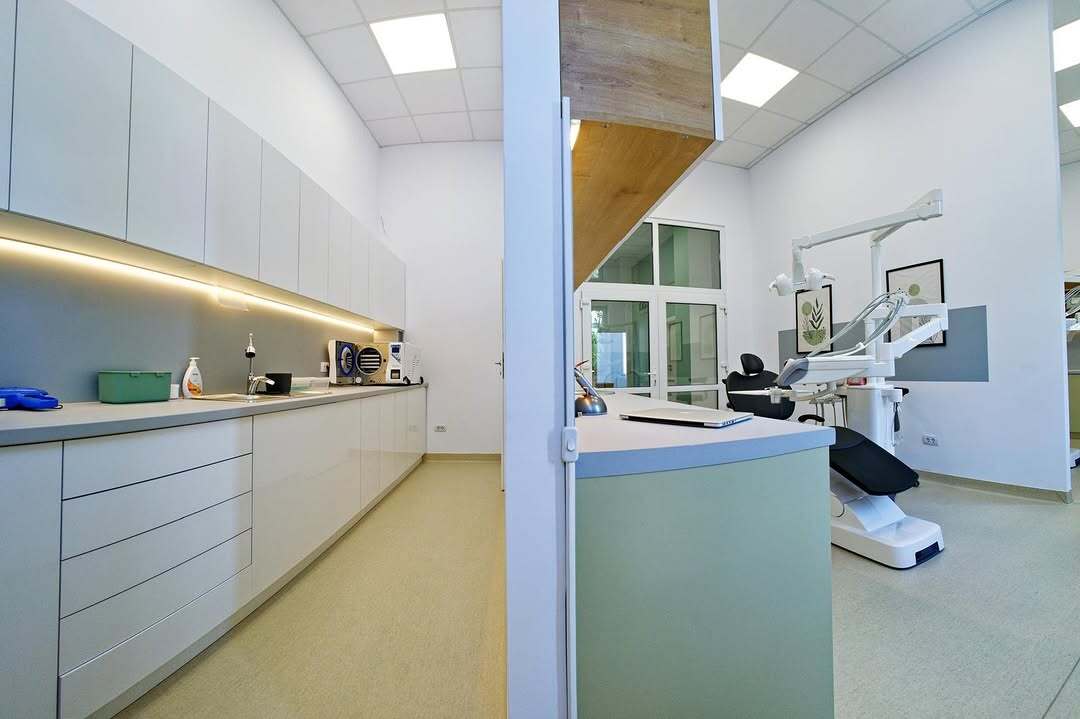 Interiorul Erste Clinic: în stânga, zona de sterilizare cu dulapuri albe; în dreapta, blatul verde-salvie și cabinetul cu unitul dentar