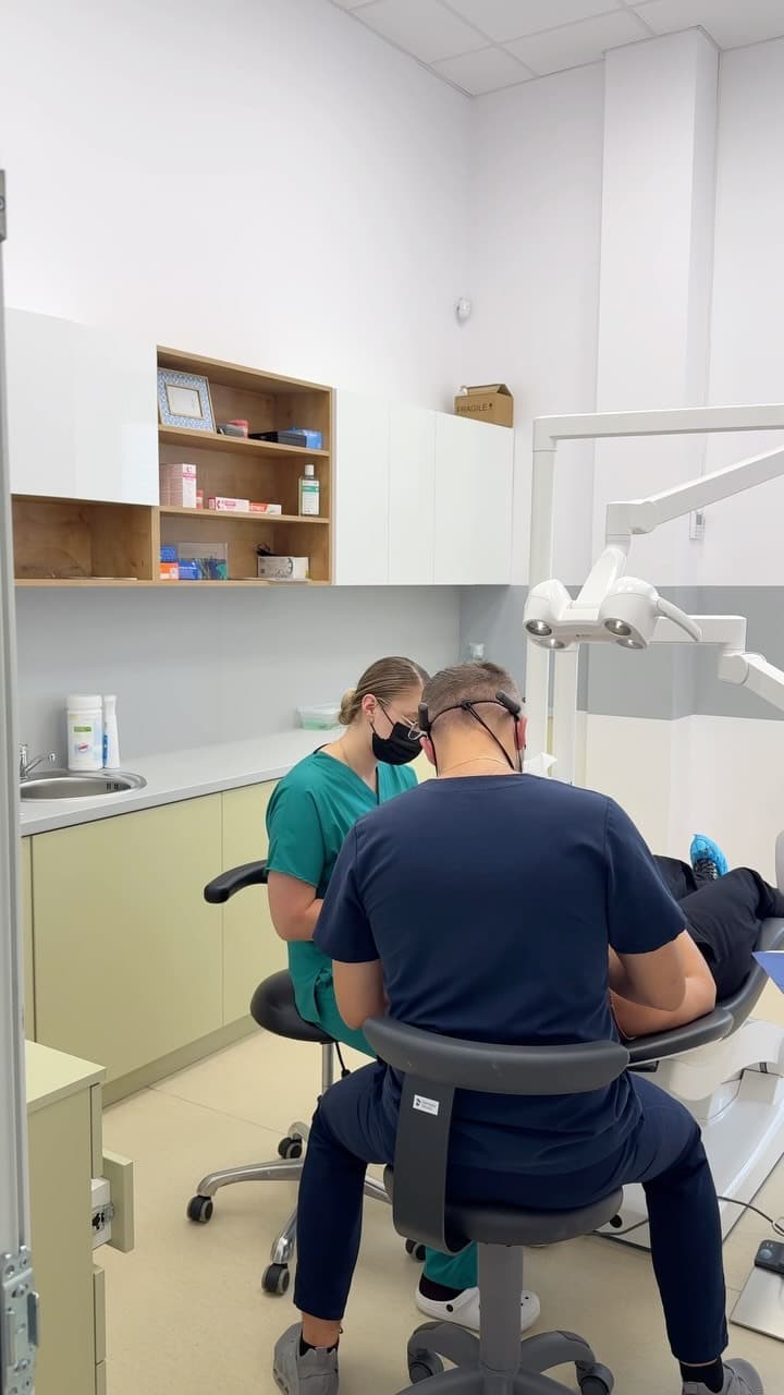 Un medic și o asistentă lucrând la unitul dentar, lângă rafturi din lemn